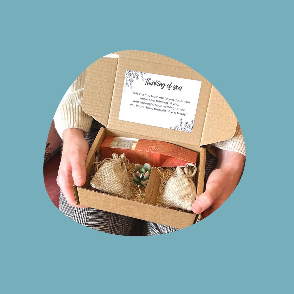 Hands holding an open gift box with candle, reed diffusers and other goodies.