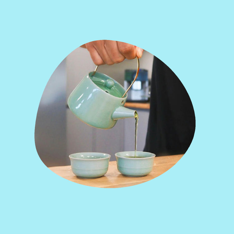 Men pouring herbal tea from a ceramic green teapot into a matching tea cup.