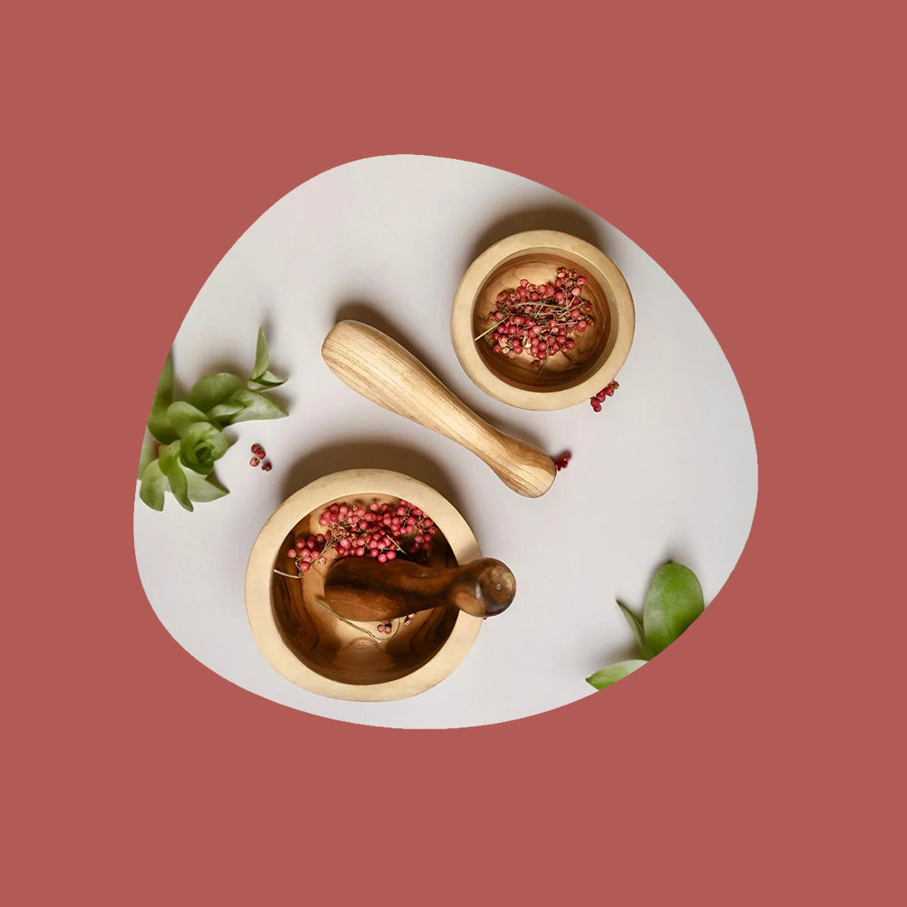 a pair of wooden eco friendly pestle and mortar with dried red herbs.