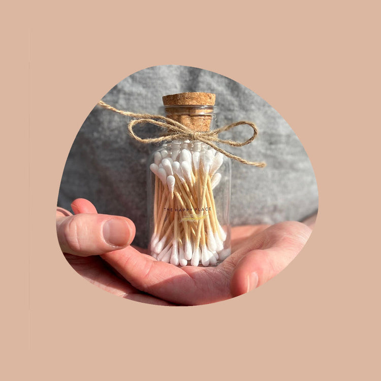 hands holding an eco friendly cotton buds in a glass jar with hessian string ribbon tied to it with a cork lid.