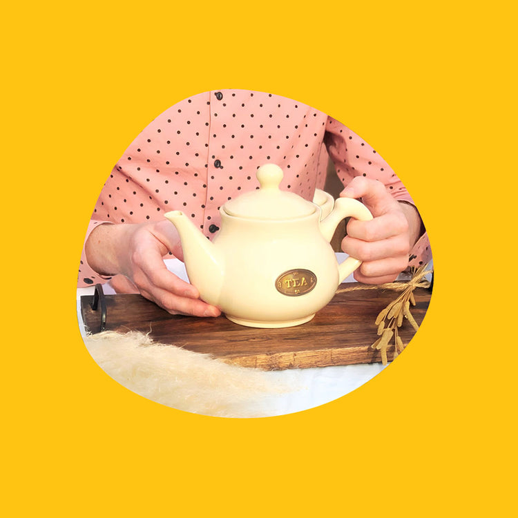 Hands Holding Teapot with rustic tablescape decorated with dried plants and flowers.