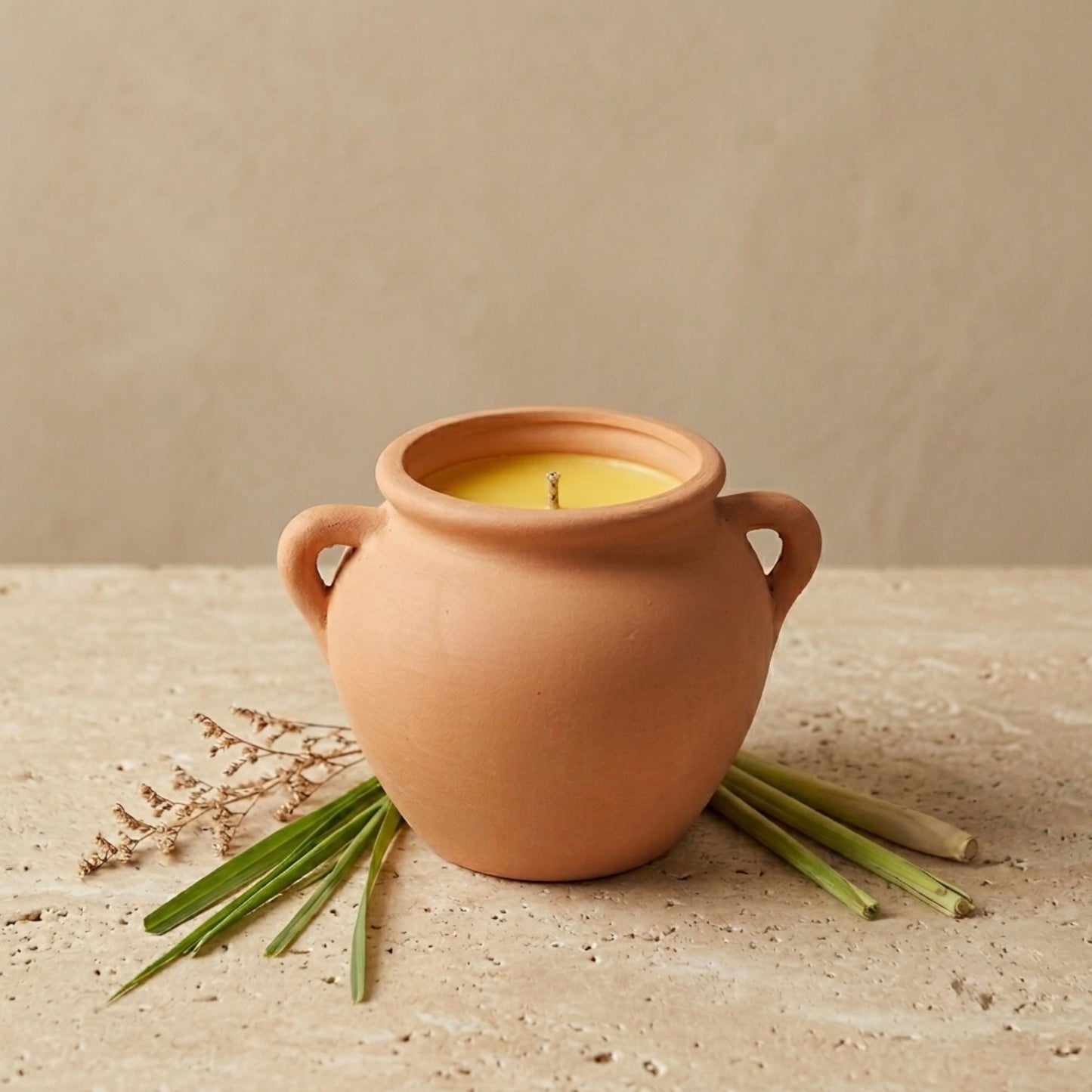 Terracotta pot with a candle on a beige surface with green leaves