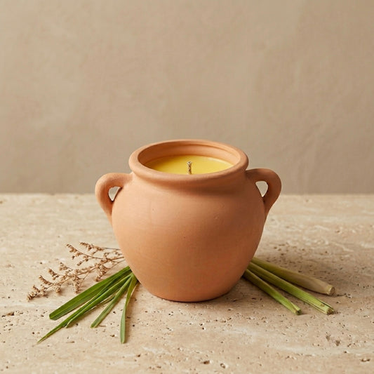 Terracotta pot with a candle on a beige surface with green leaves