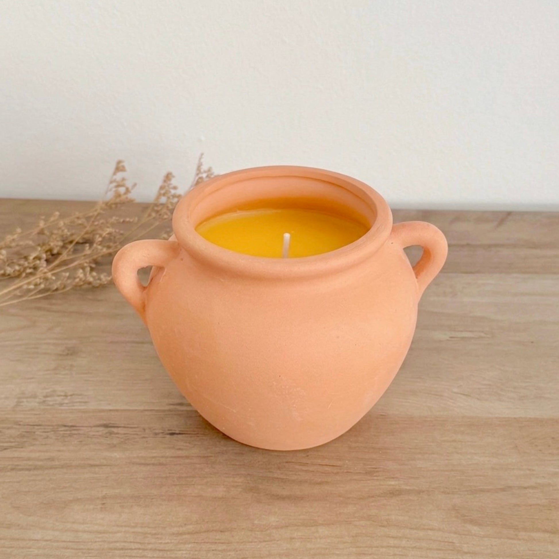 Terracotta pot candle on a wooden surface with dried plants in the background