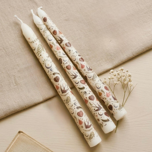 Three decorated painted candles with floral patterns on a beige surface.