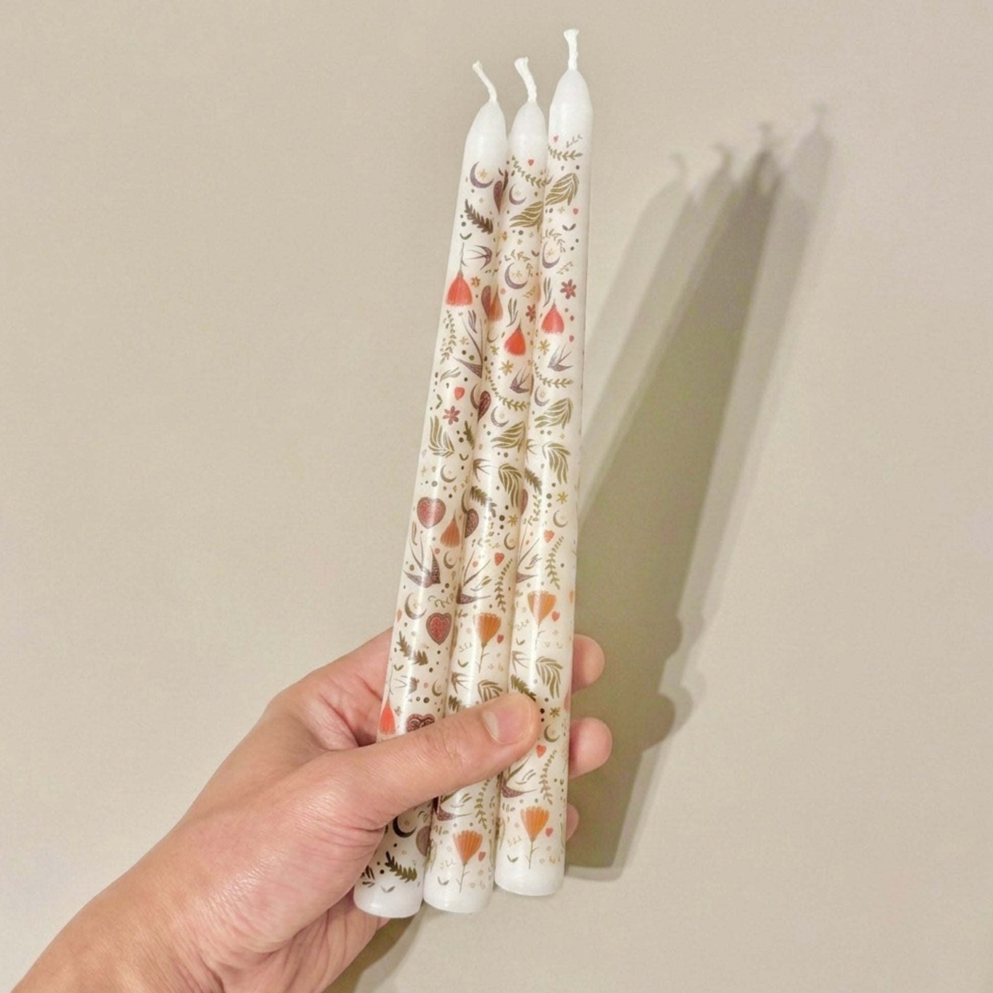 Hand holding four patterned candles against a plain background