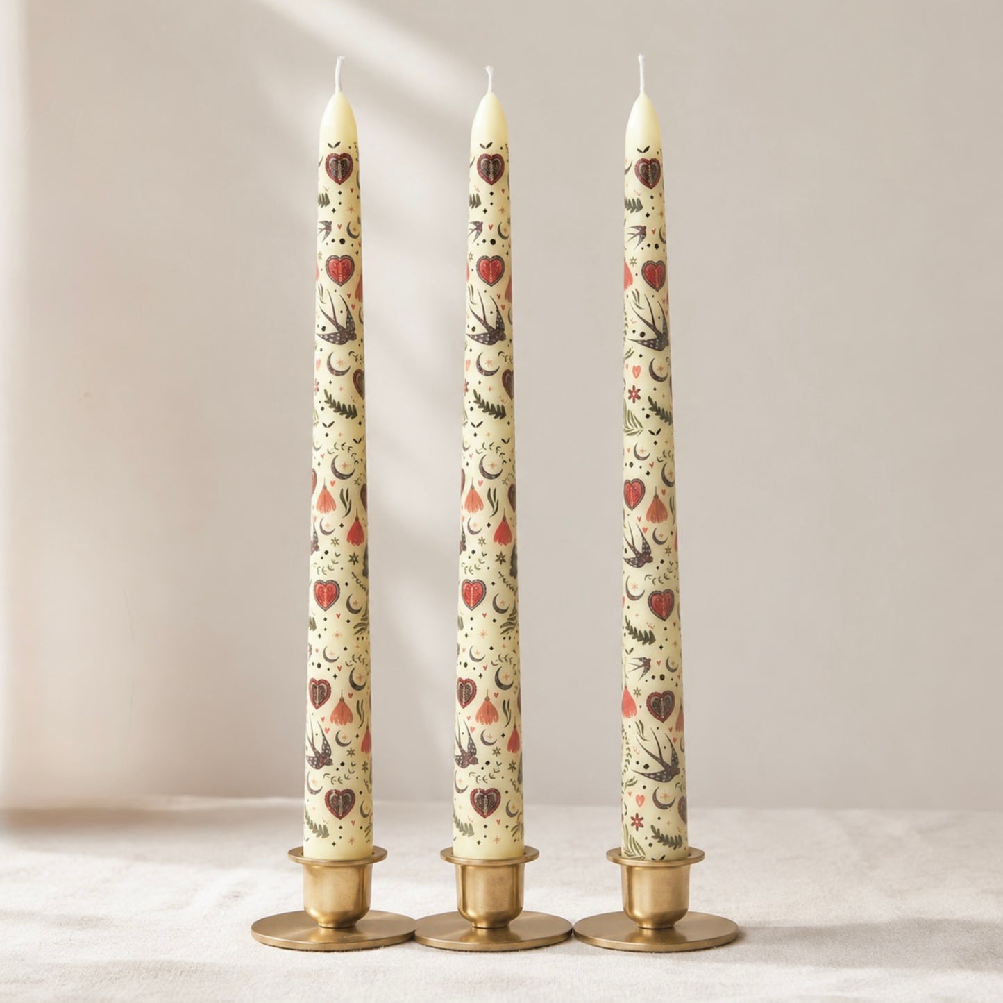 Three tall taper candles with decorative patterns on a neutral background