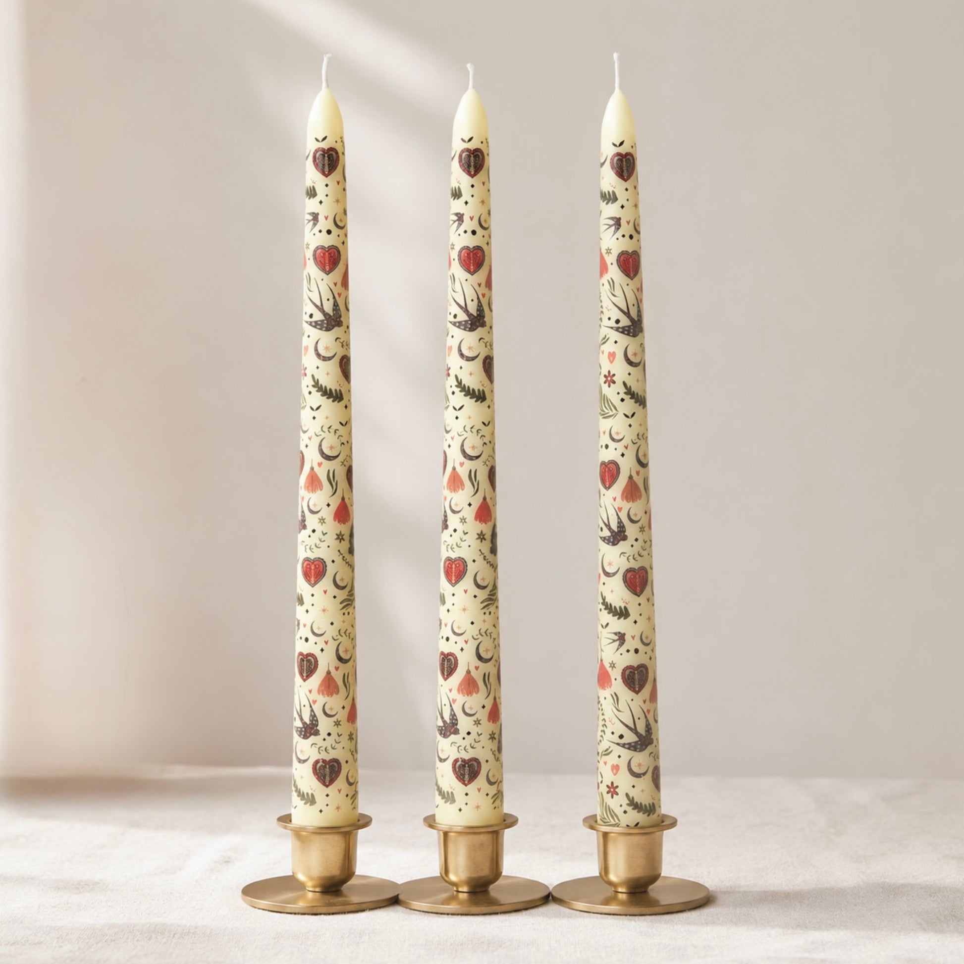 Three tall taper candles with decorative patterns on a neutral background