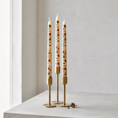 Three decorative taper candles with gold holders on a white surface against a light gray wall.