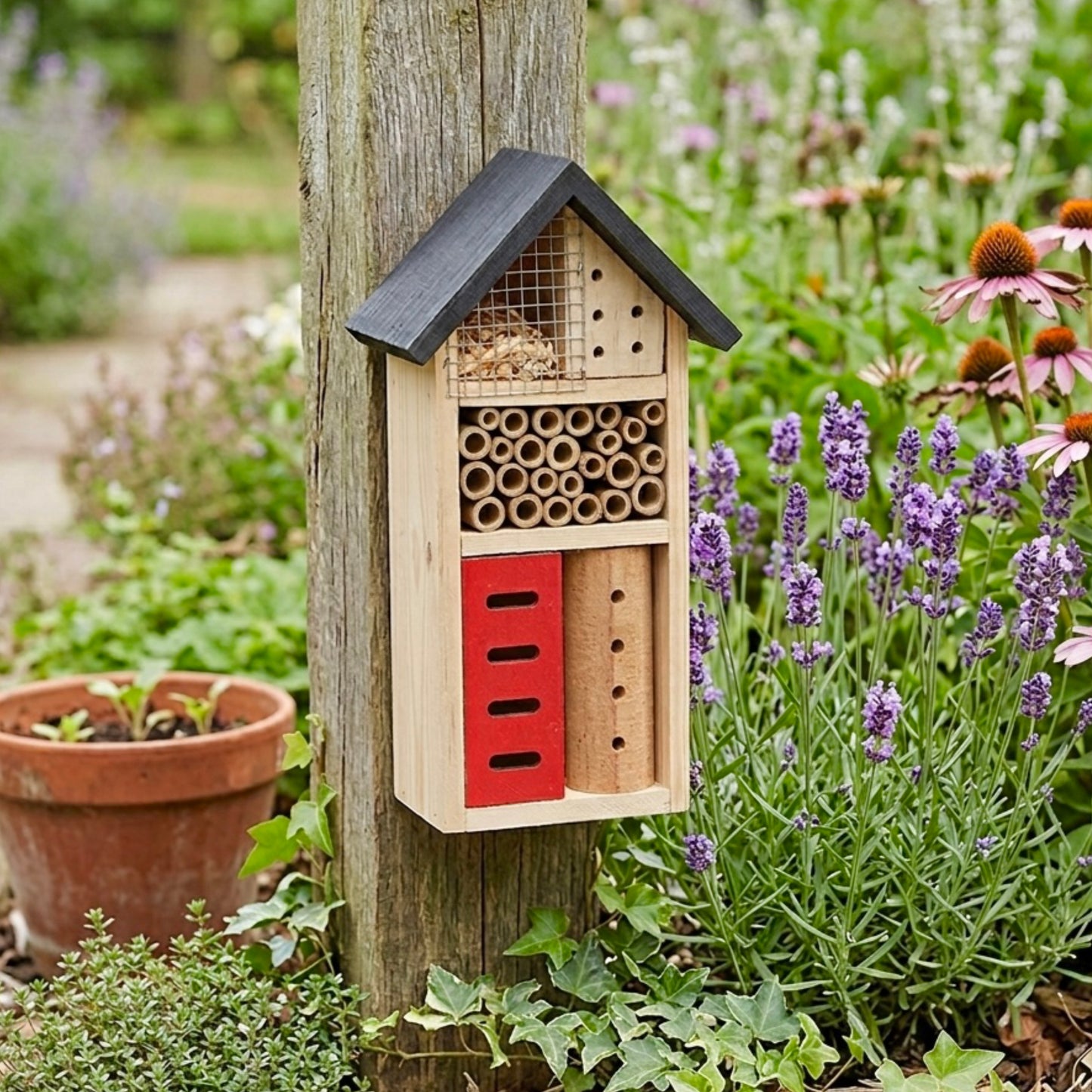 Wooden bee house attached to a tree trunk with flowers and plants in the background