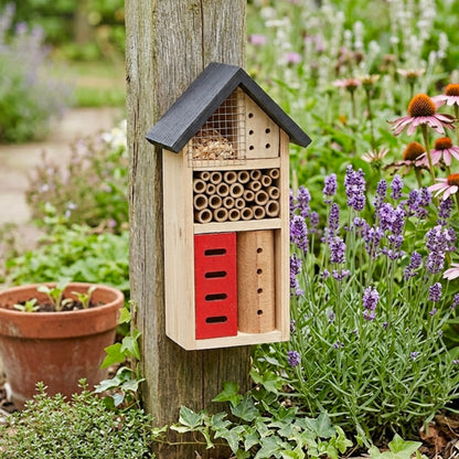 Wooden bee house attached to a tree trunk with flowers and plants in the background