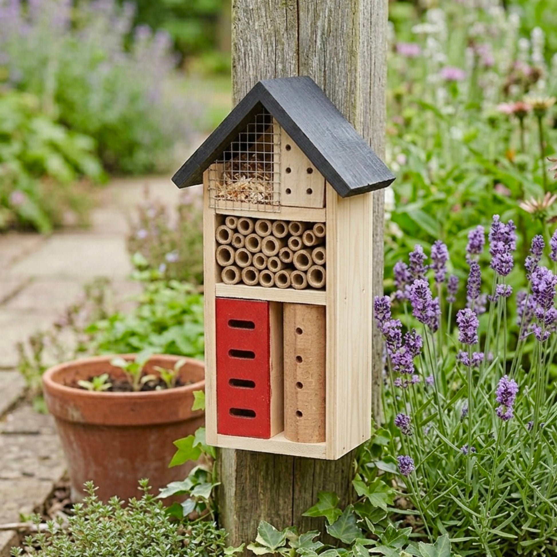 Insect hotel attached to a wooden post with lavender and flowers in the background