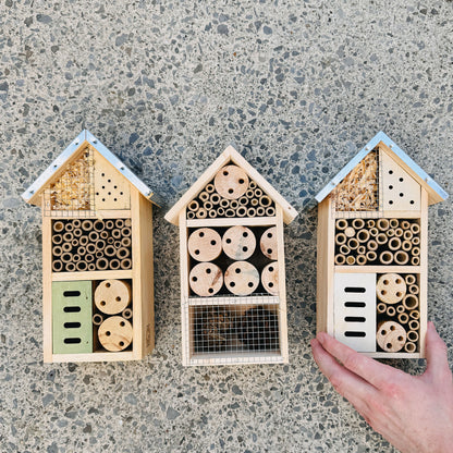 Three wooden bee hotels on a concrete surface with a hand holding one of them.