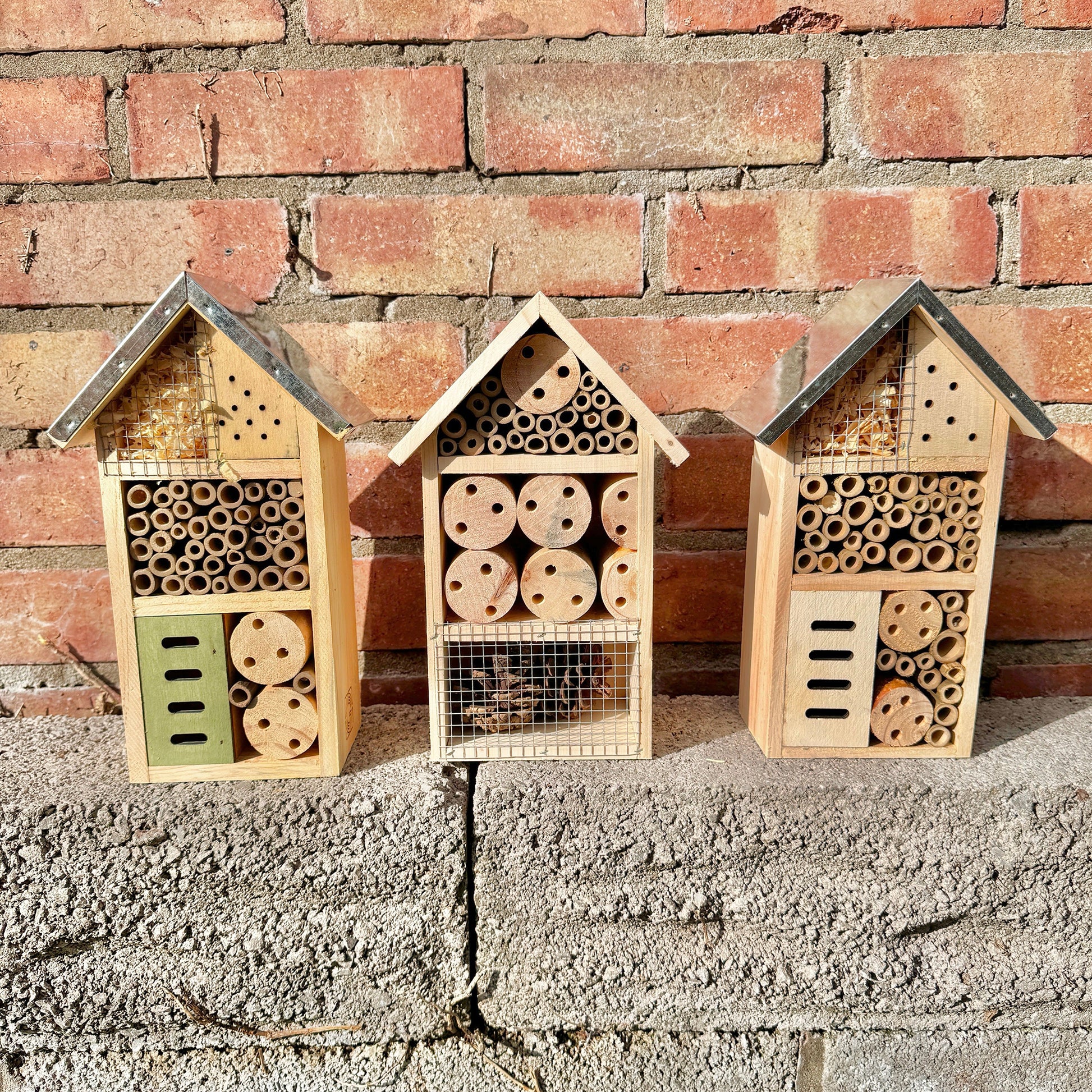 Three wooden bug hotels against a brick wall.