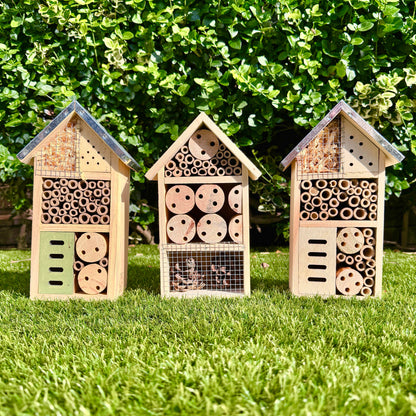 Three wooden bee hotels on grass with a green bush background