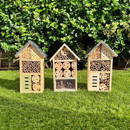 Three wooden insect hotels on grass with a green bush background